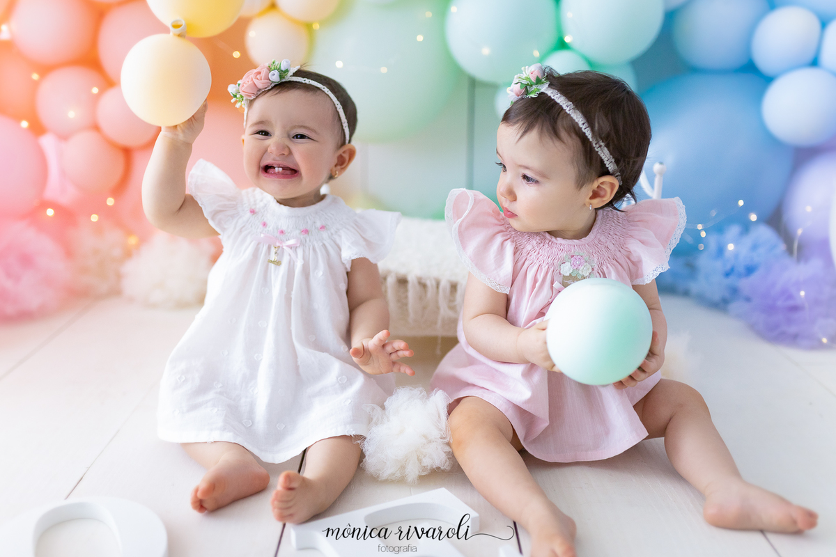 No cenário de Smash The Cake, as duas bebês estão sentadas uma ao lado da outra, cada uma está segurando um balão. Uma delas está sorrindo e levantando o balão e a outra está olhando para o lado
Fotografado por Mônicas Fotografia em Maringá-PR
