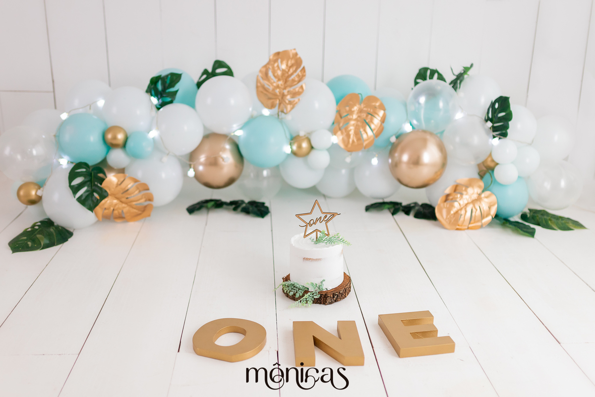 A foto mostra um cenário de uma sessão de Smash The Cake. No centro tem um bolo branco com uma estrela no topo, na frente está a palavra 