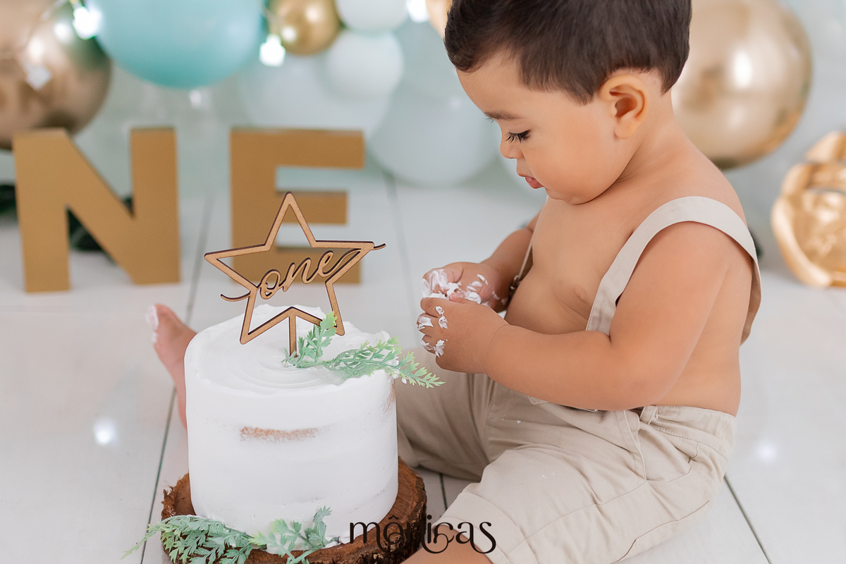 No cenário de Smash, o bebê Caio está sentado de lado com o bolo entre as pernas, as mãos estão sujas de bolo e ele está olhando para elas. Ele está explorando a textura do chantilly.
Fotografado por Mônicas Fotografia em Maringá-PR