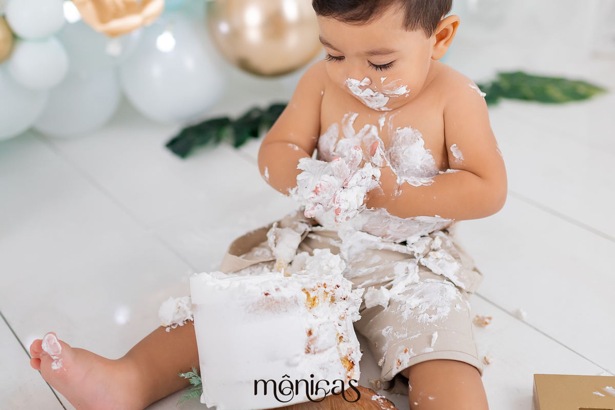 No cenário de Smash, o bolo está na frente do bebê, que está todo lambuzado de chantilly e olhando para as mãos enquanto sente a textura.
Fotografado por Mônicas Fotografia em Maringá-PR