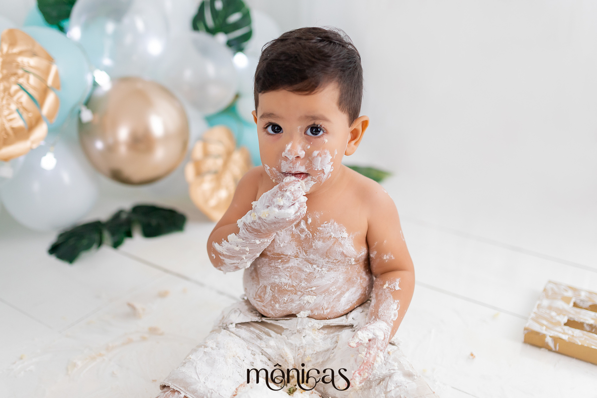 No cenário de Smash, o bebê está todo lambuzado de chantilly. Ele está levando para a boca um pedaço de bolo para experimentar o sabor.
Fotografado por Mônicas Fotografia em Maringá-PR