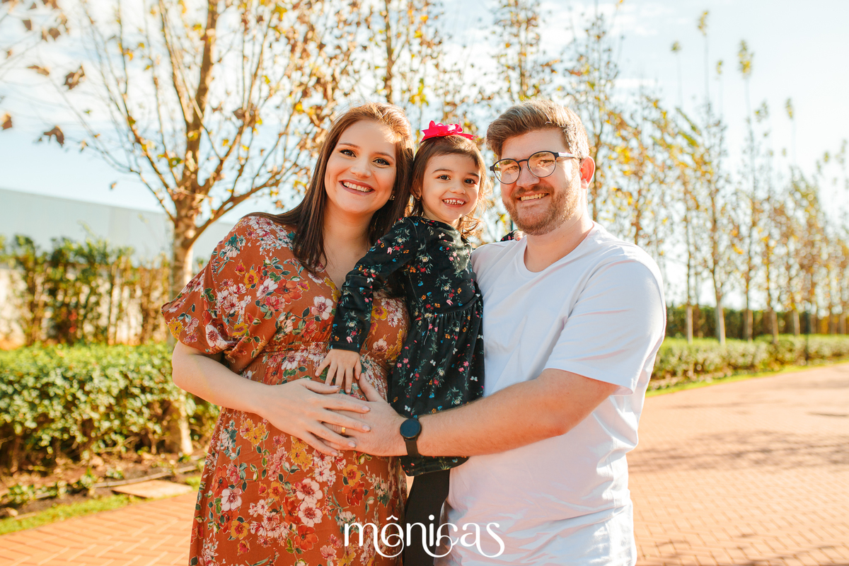Uma foto da família! mãe grávida, filha mais velha e pai estão srrindo. A filha mais velha está no colo do pai que abraça a todas