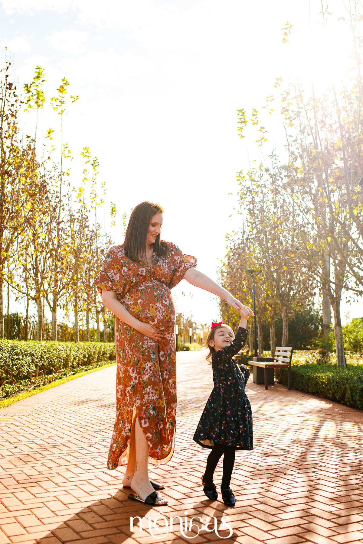 Com a filha mais velha, a gestante caminha em uma parque e brinca de rodar com sua filha
