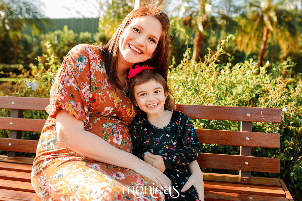 Sentadas em um banco no Eurogarden em Maringá, a gestante e sua filha mais velha se abraçam e sorriem para a fotógrafa Mônica
