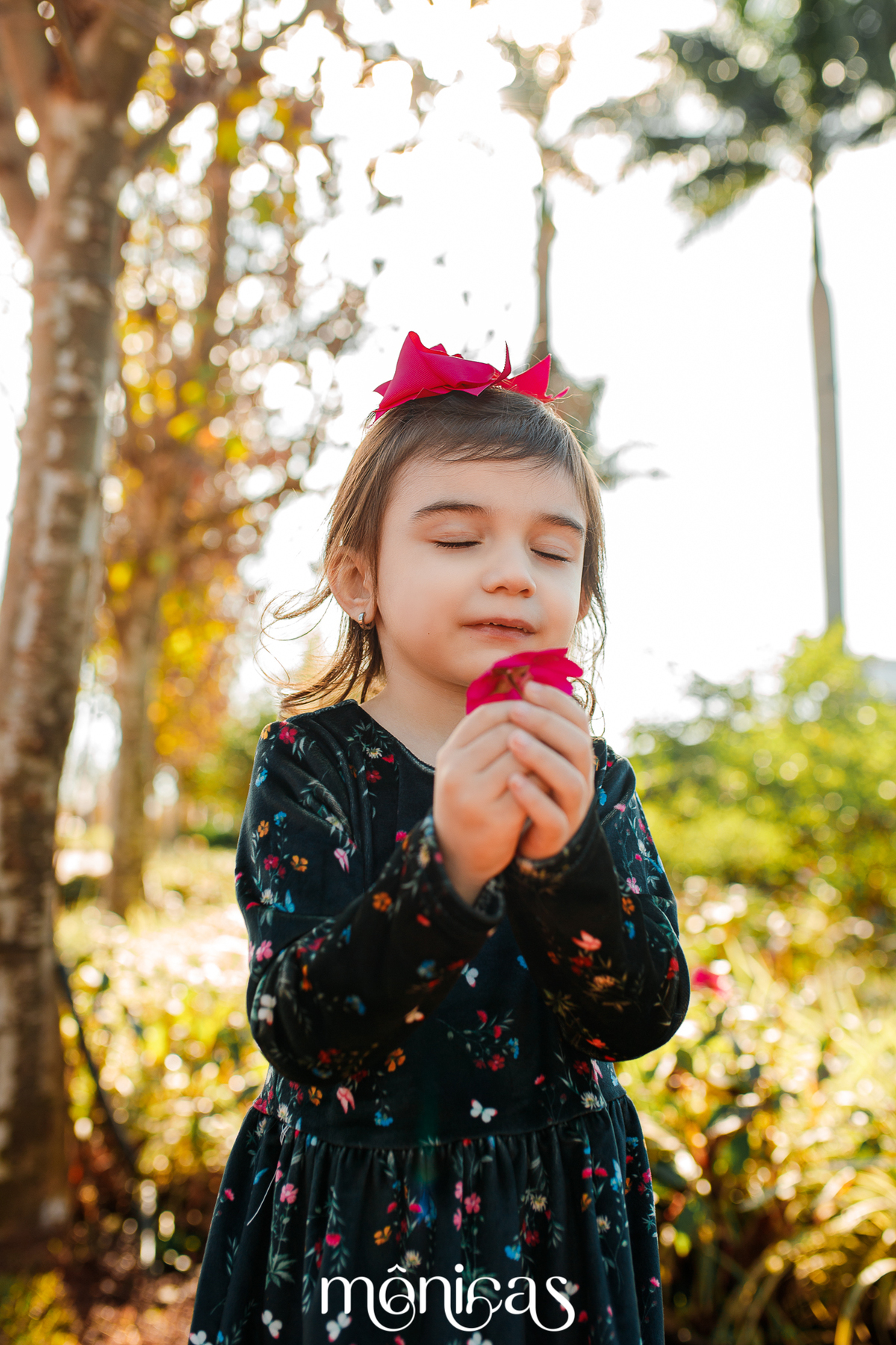 Iluminada pelo sol, a irmã mais velha chamada Liz segura uma flor em suas mãos e suspira como se sentisse o cheiro da florzinha