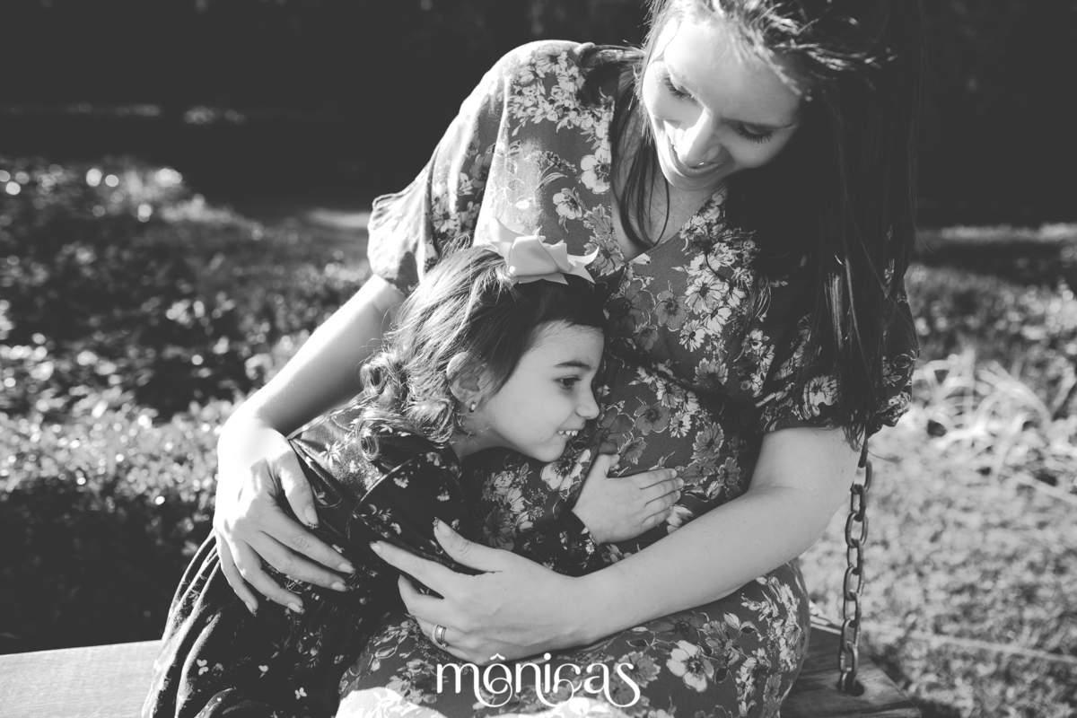 Sentada em um banco com a mãe, a irmã mais velha abraça a barriga da mãe que etá grávida