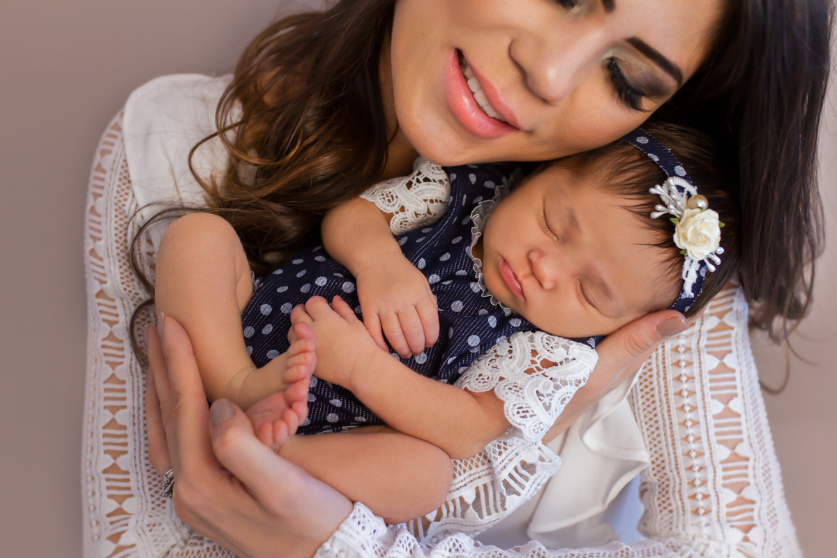 Segurando a Gabi nos braços, a mamãe encosta seu rosto da bochecha da Gabi e sorri