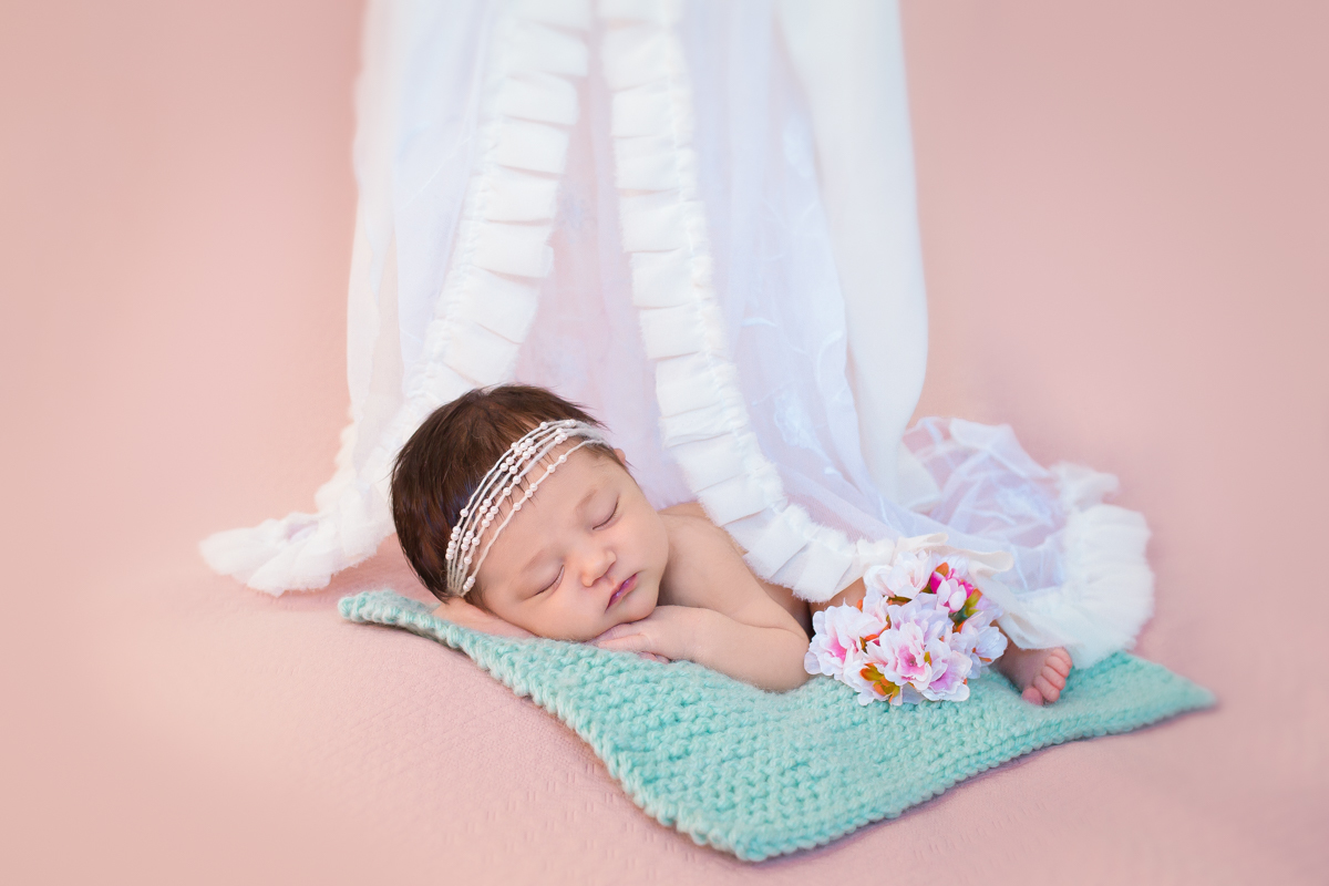 Deitadinha com as mãos no queixo, a Gabriela dorme em um tapetinho verde de tricô. Ao lado, uma flor de cerejeira que faz referência à sua descendência e um dossel por cima dela