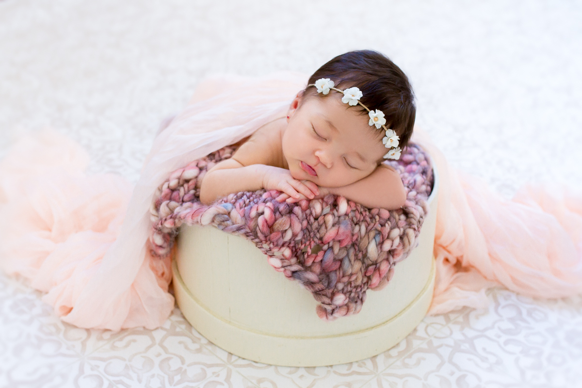 Em um fundo de tecido, a Gabi dorme dentro de um cestinho, item muito usado na fotografia newborn