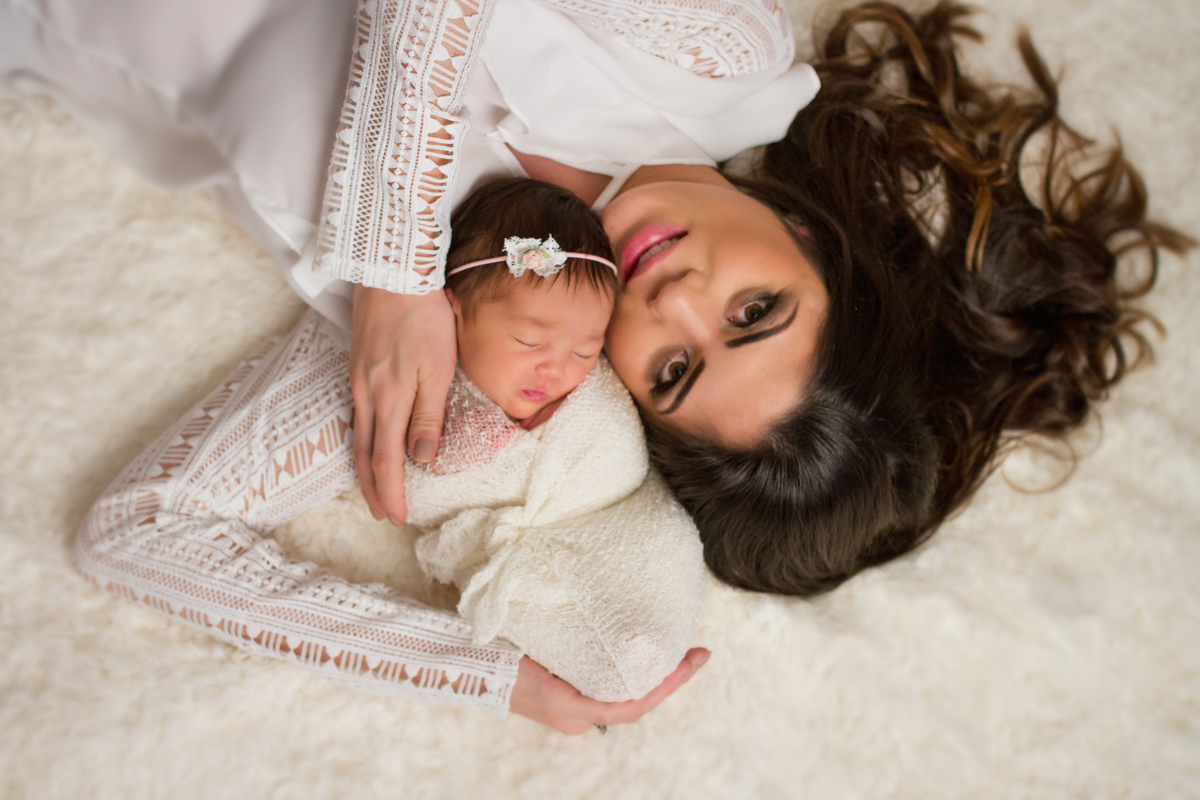 A Gabi e a mamãe estão deitadas em um pêlo branco bem fofinho. A mamãe segura a bebê nos braços