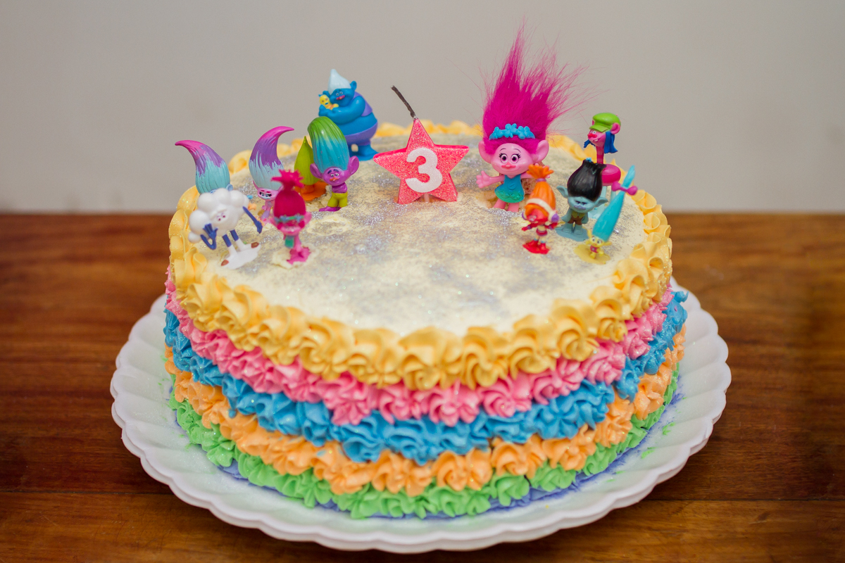 Aqui está o bolo com seis cores e os bonecos do filme Trolls como decoração