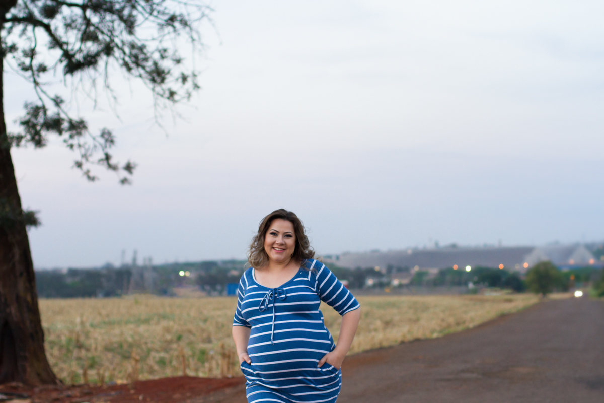  A gestante está com um vestido azul listrado de branco e caminha com as mãos no bolso.