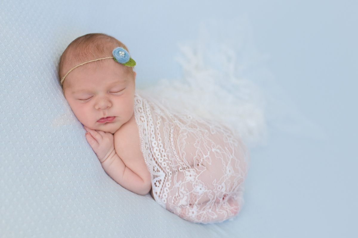 Enroladinha em uma renda linda, a Isadora está deitada de bruços com a mão no queixinho