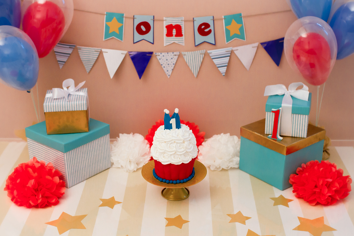 Detalhes do cenário. Aqui temos caixas de presente, bexigas, bandeirolas e o bolo com uma coroa
