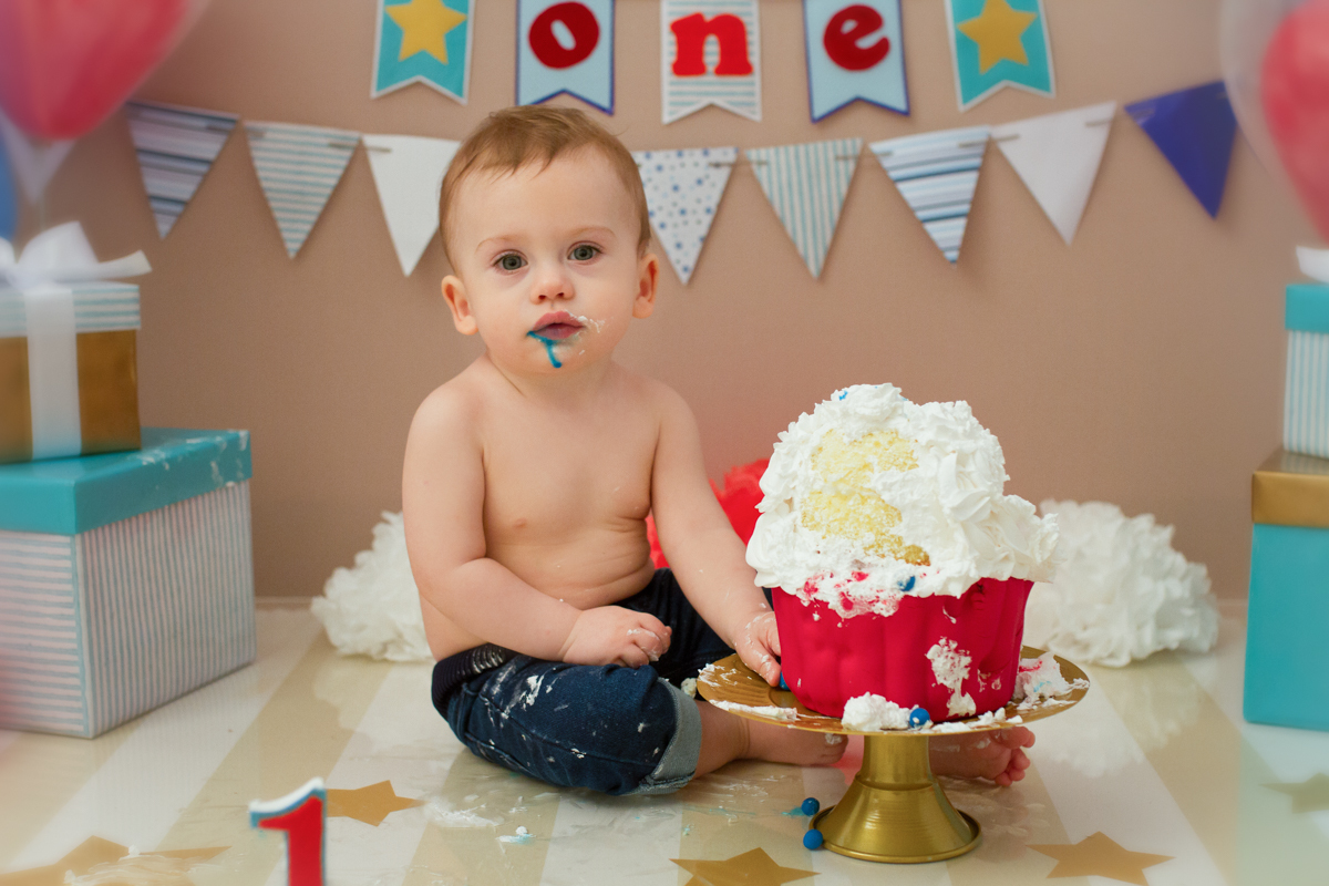 O bolo tem bolinhas de pasta americana na cor azul, nesta foto, ele come uma bolinha e fica com a boca toda suja