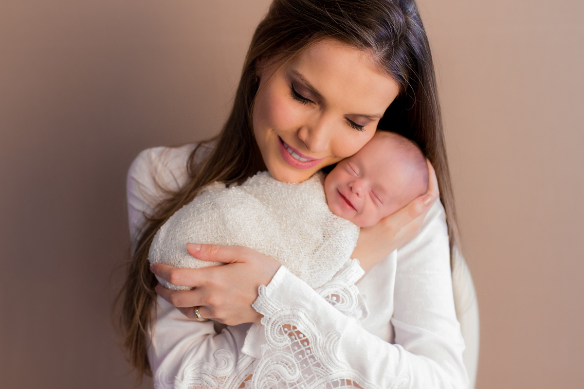 Na foto com a mamãe segurando-o em seus braços, em um fundo marrom, ele sorri.
