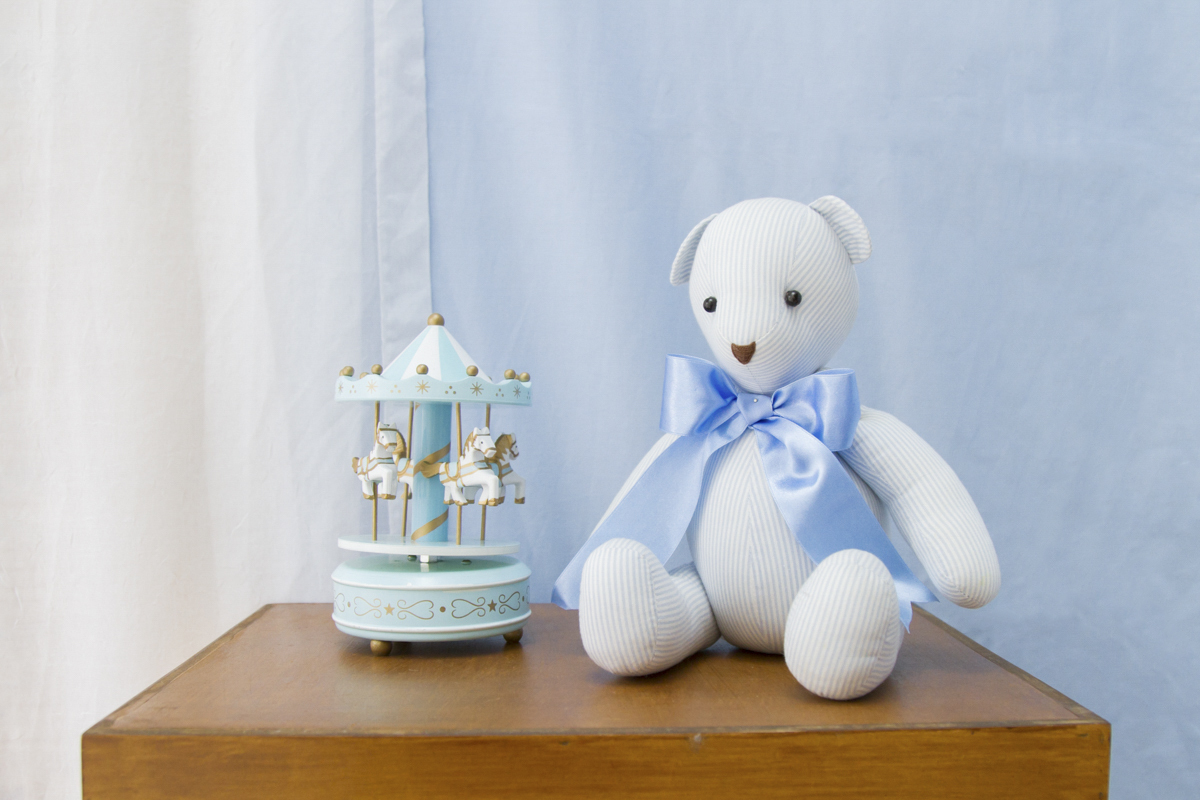 Ursinho do lacinho azul e acompanhado de um mini carrossel do lado, que também é azul