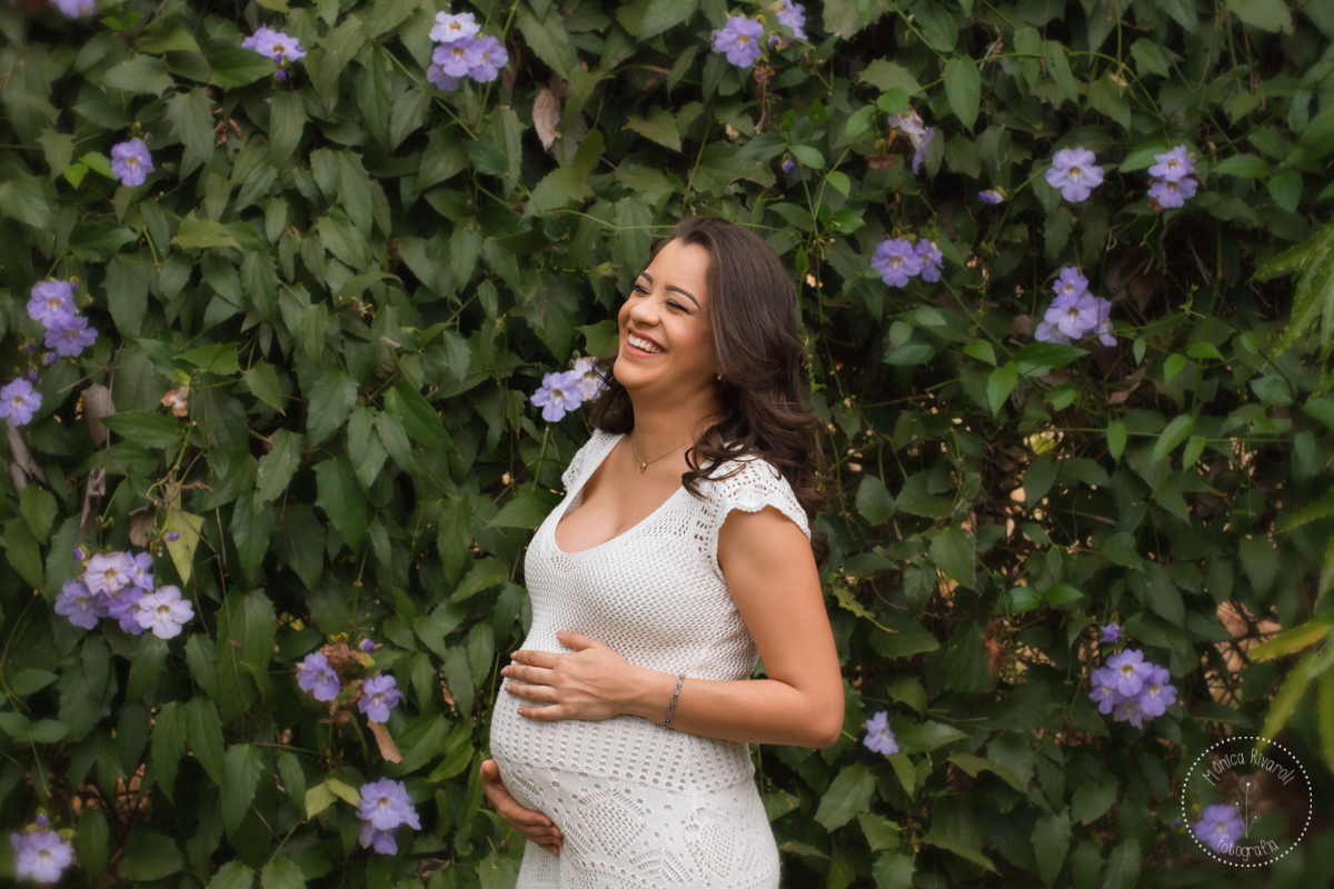 Em meio à flores roxas, a Mari sorri com a mão na barriga