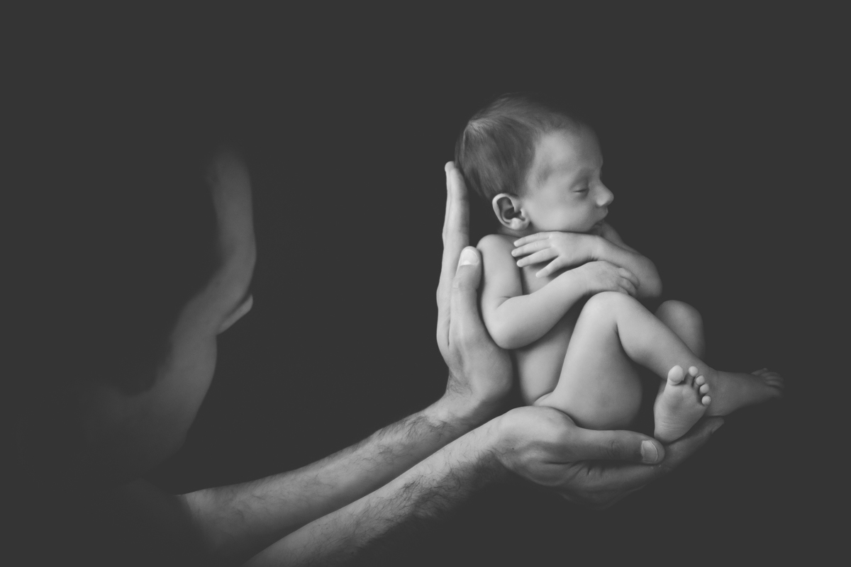 Em uma foto preto e branco, o papai segura o Dudu com as mãos e na foto aparece a sombra do rosto do papai bem próximo do rostinho do Dudu.