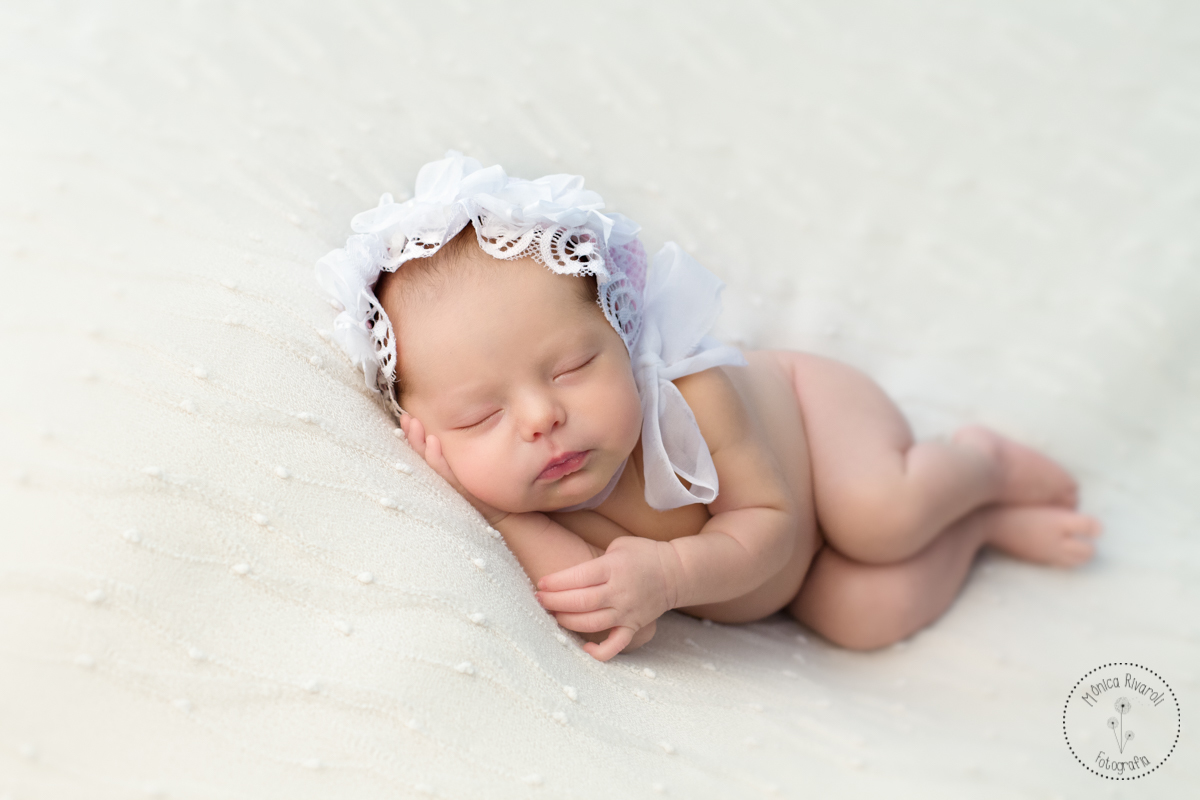 Com uma touquinha de tecido, a Laura está deitadinha de lado com a mão apoiada no queixinho