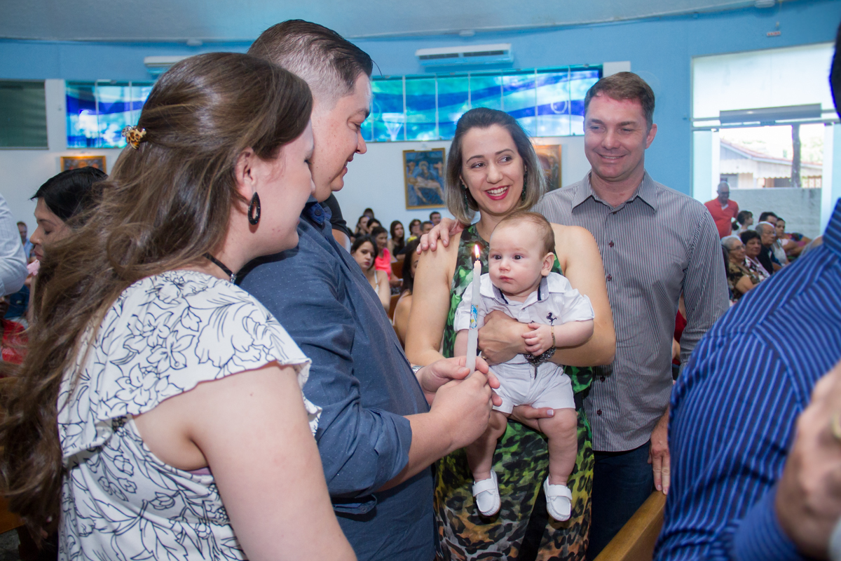 Agora o Miguel está no colo da madrinha e olhando para a vela que está com o papai