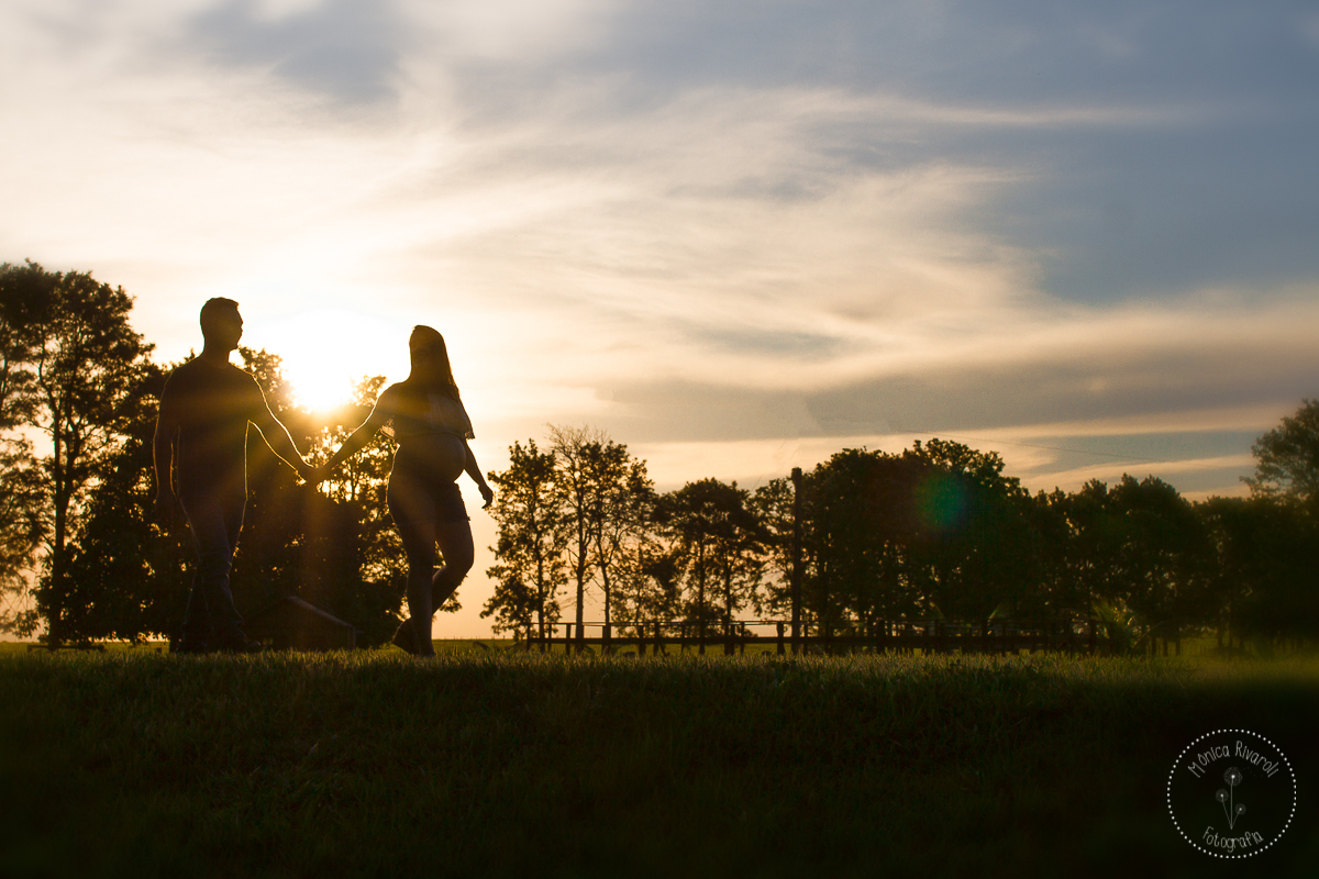 O casal andando de mãos dadas e no fundo um lindo por do sol e arvores
