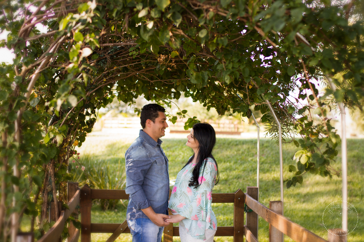 Sob um túnel de trepadeiras, a Andressa e o Rafa estão de frente um para o outro se olhando e com as mãos dadas
