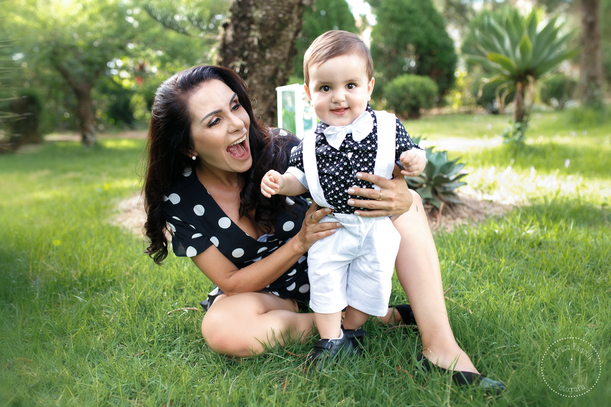 O Henrique esta de pé do ladinho da mamãe, que esta sentada na grama