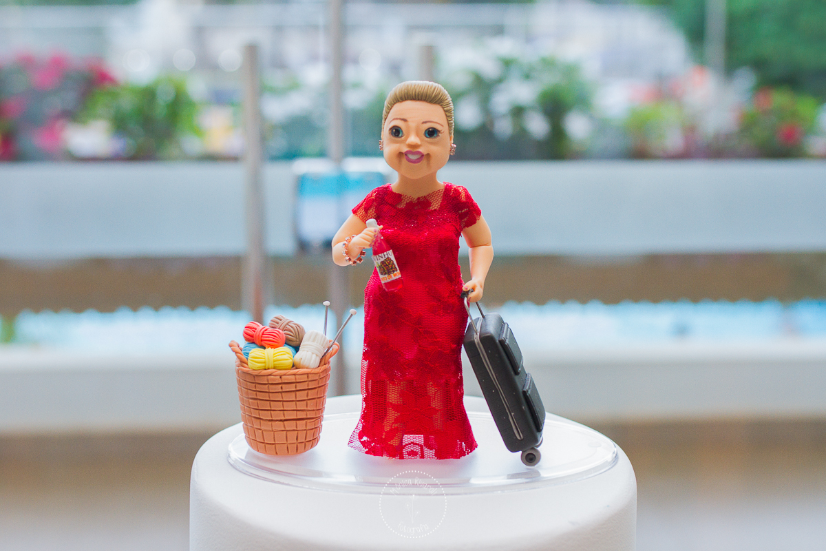 Bonequinha inspirada na d. Dalva, segurando um vinho e ma mala ao lado de um cesto de tricô 