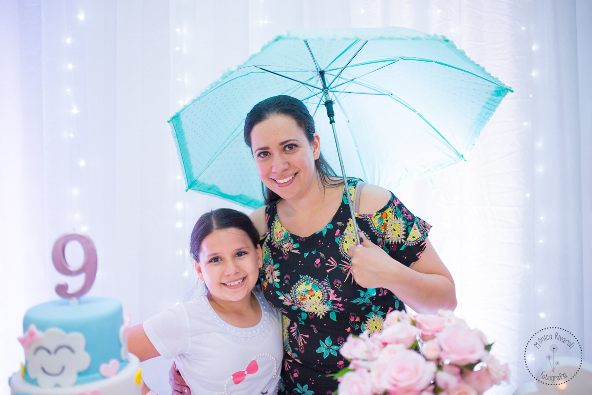 Nicoli e a mamãe, atrás da mesa de doces, com um guarda-chuva da decoração