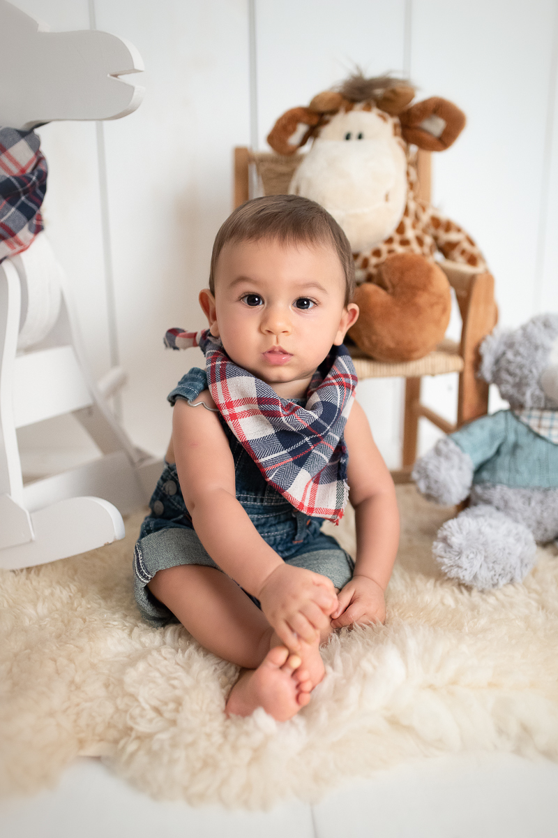 O Eduardo está segurando os pezinhos e olhando para frente. Ele veste um macacão jeans e usa a bandana xadrez igual ao cavalinho