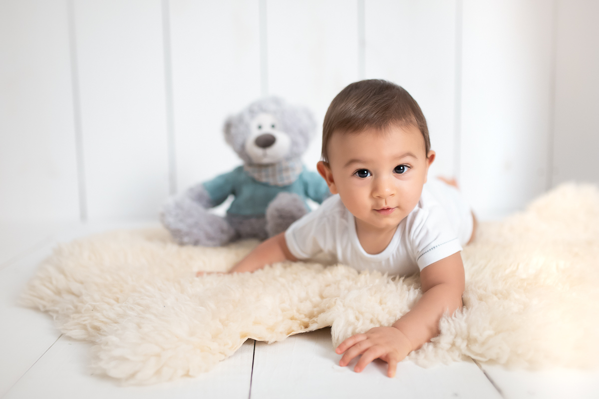 De bruços e ao lado do urso, o Edu olha para a foto e sorri