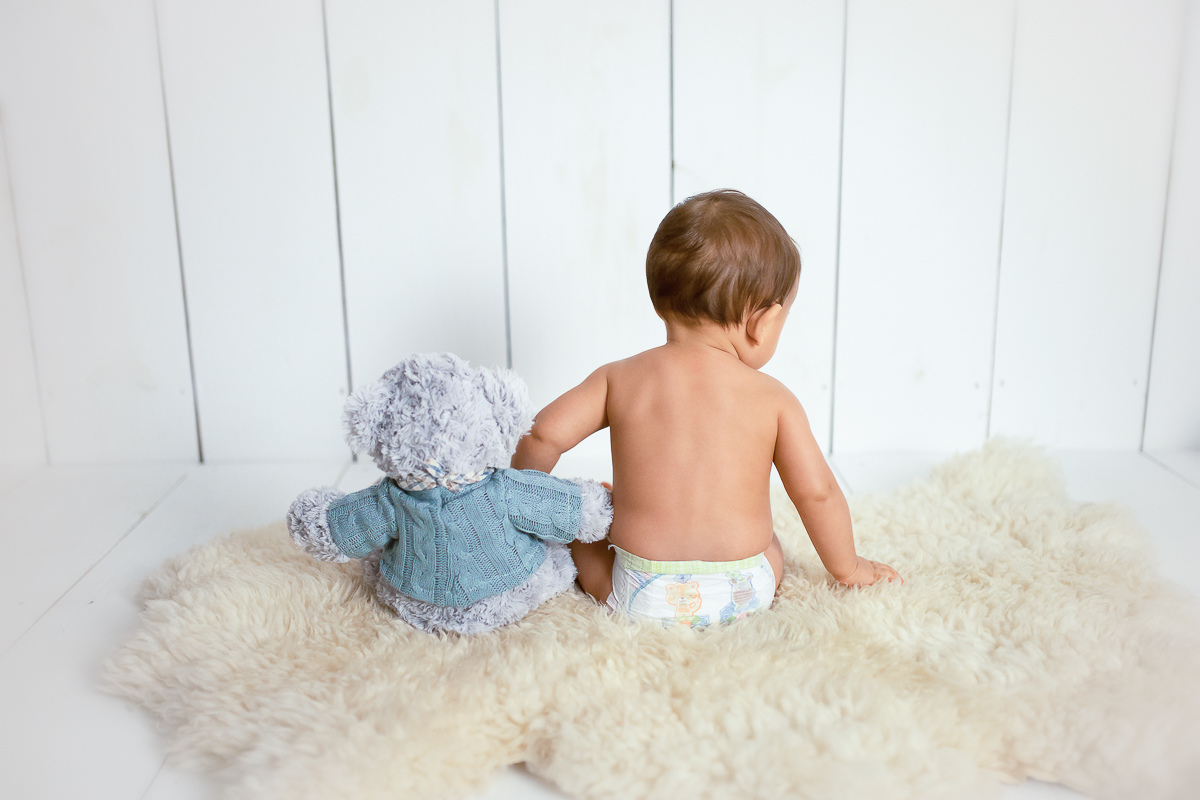 Viradinho de costas com a fraldinha aparecendo, o Edu dá a mãozinha para seu amigo urso que também está virado de costas