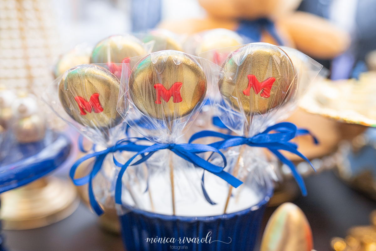 Docinho dourado no palito, com a letra M, em dourado 