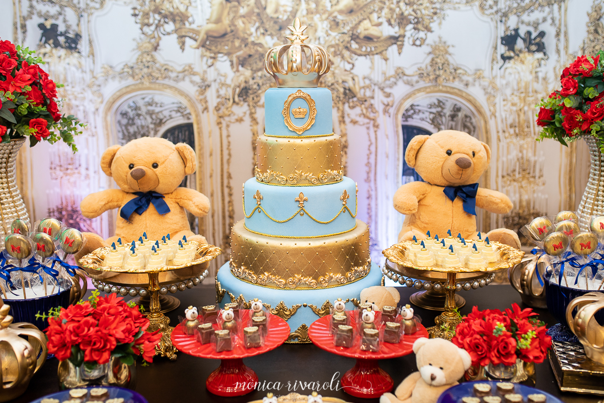 Close no bolo de quatro andares, azul claro e dourado, dos dois lados do bolo, um urso amarelo com lacinho azul no pescoço