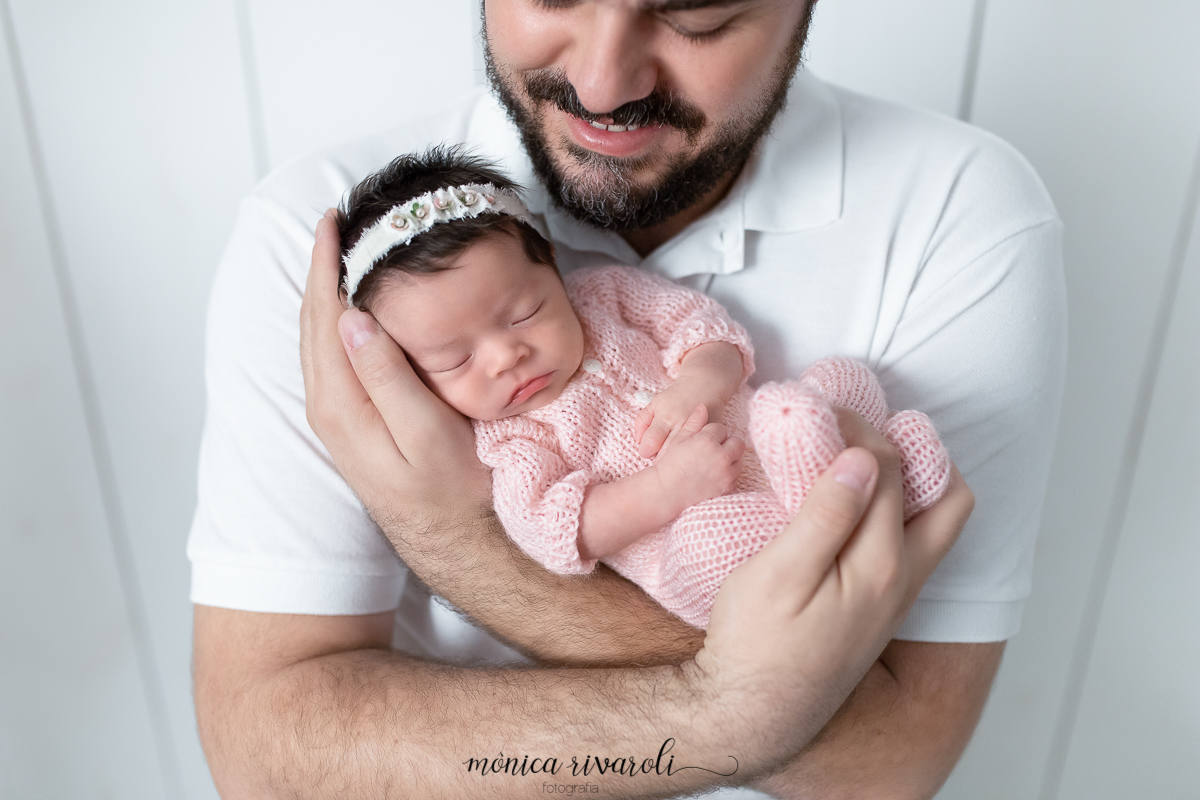 Foto com o papai segurando a bebê no colo. O pai está olhando para a bebê e ele tem o rosto cortado para melhor foco na foto