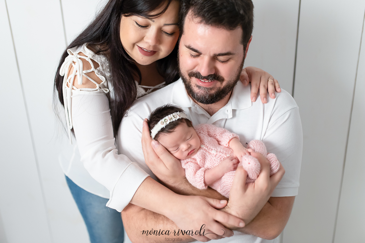 Foto com a mãe e o pai. Ambos estão olhando para a bebê que dorme tranquila