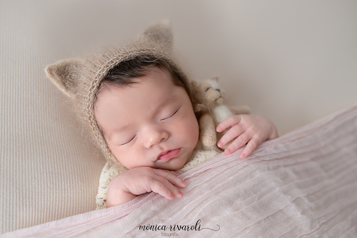 A bebê está com uma touquinha de gatinho e coberta por uma mantinha como se estivesse dormindo na sua caminha