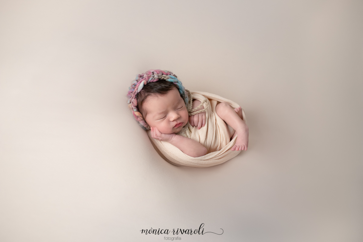Como se fosse um casulinho, a bebê está enroladinha em um tecido fofinho com os pezinhos e as mãozinhas enroladinhas. Esta pose é semelhante à maneira que os bebês se encontram no útero da mamãe