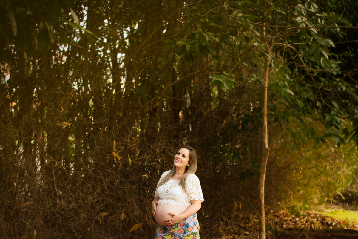 Em um jardim com folhas secas, a mamãe sorri ao sentir sua bebe