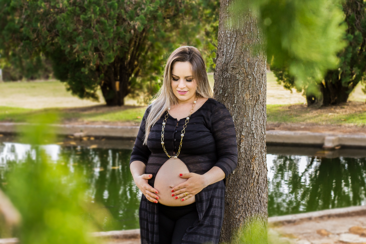 Encostada em uma árvore, a mamãe olha para seu ventre, feliz em aguardar sua be
