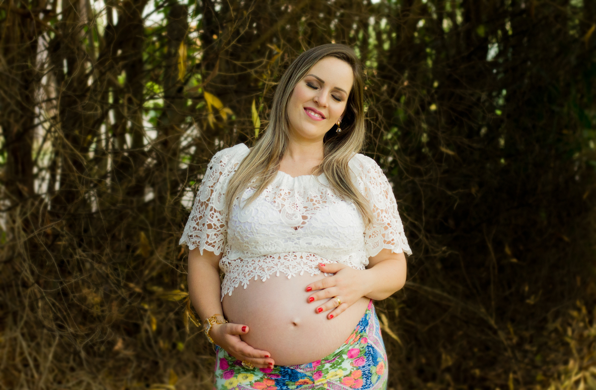 Com uma blusa mostrando a barriga, a mamãe sente sua bebê em seu ventre e sorri