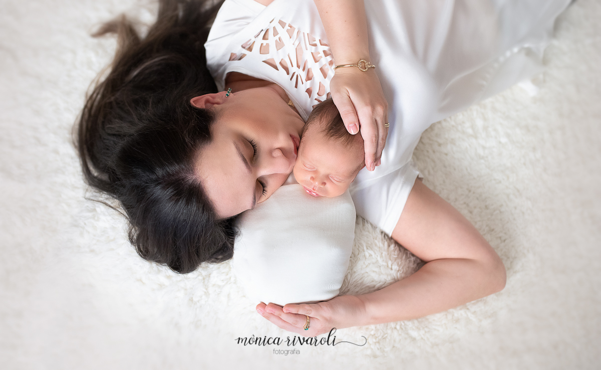 Breno aqui esta com um wrap branco deitado carinhosamente no colo da mamãe recebendo um beijo com muito amor. Ensaio feito pelas melhores fotografas de Maringá/PR Monica Rivaroli Fotografia