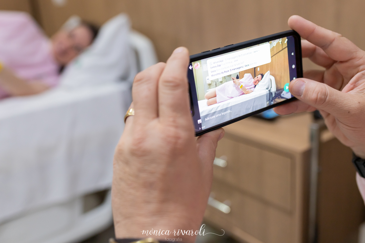 A mamães esta deitada na cama e o papai fazendo fotos pelo celular e postando nas redes sociais. @monicarivarolifotografia fotografo de parto em maringá.Hospital Paraná.