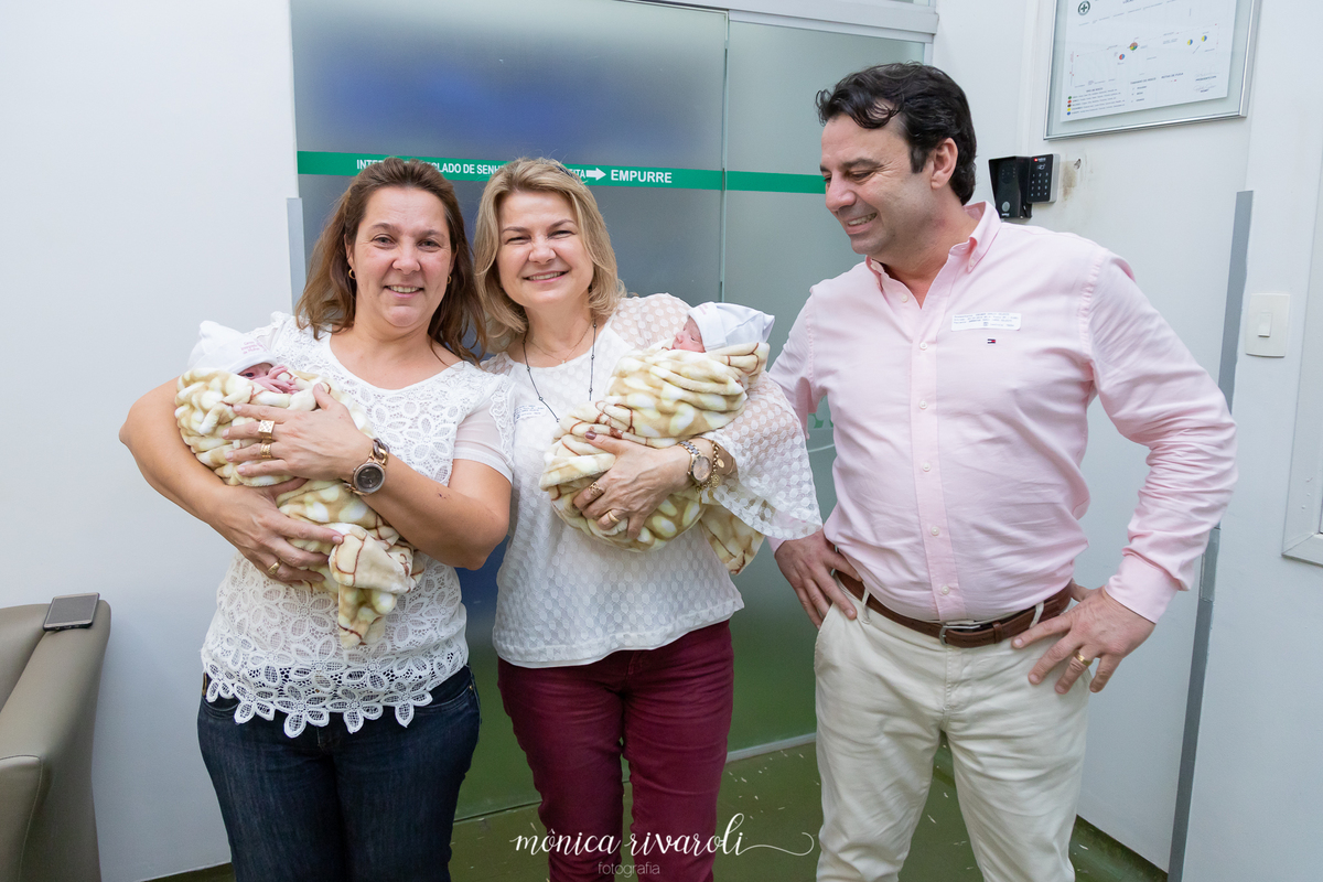 A vovó e a madrinha seguram as bebês e o papai observa ao lado!