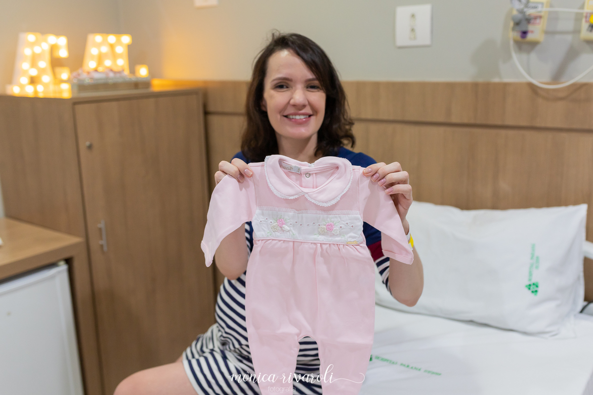 A mamãe Samantha esta segurando uma roupinha que será a saída de maternidade das meninas. 