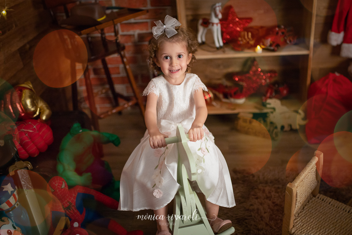 Ana Laura no cavalinho de pau.Mini sessão de Natal 2018 no estúdio Monica Rivaroli Fotografia em um quarto de brinquedos onde as crianças se divertiram muito! Agende um horário para sessão mais linda do ano!
