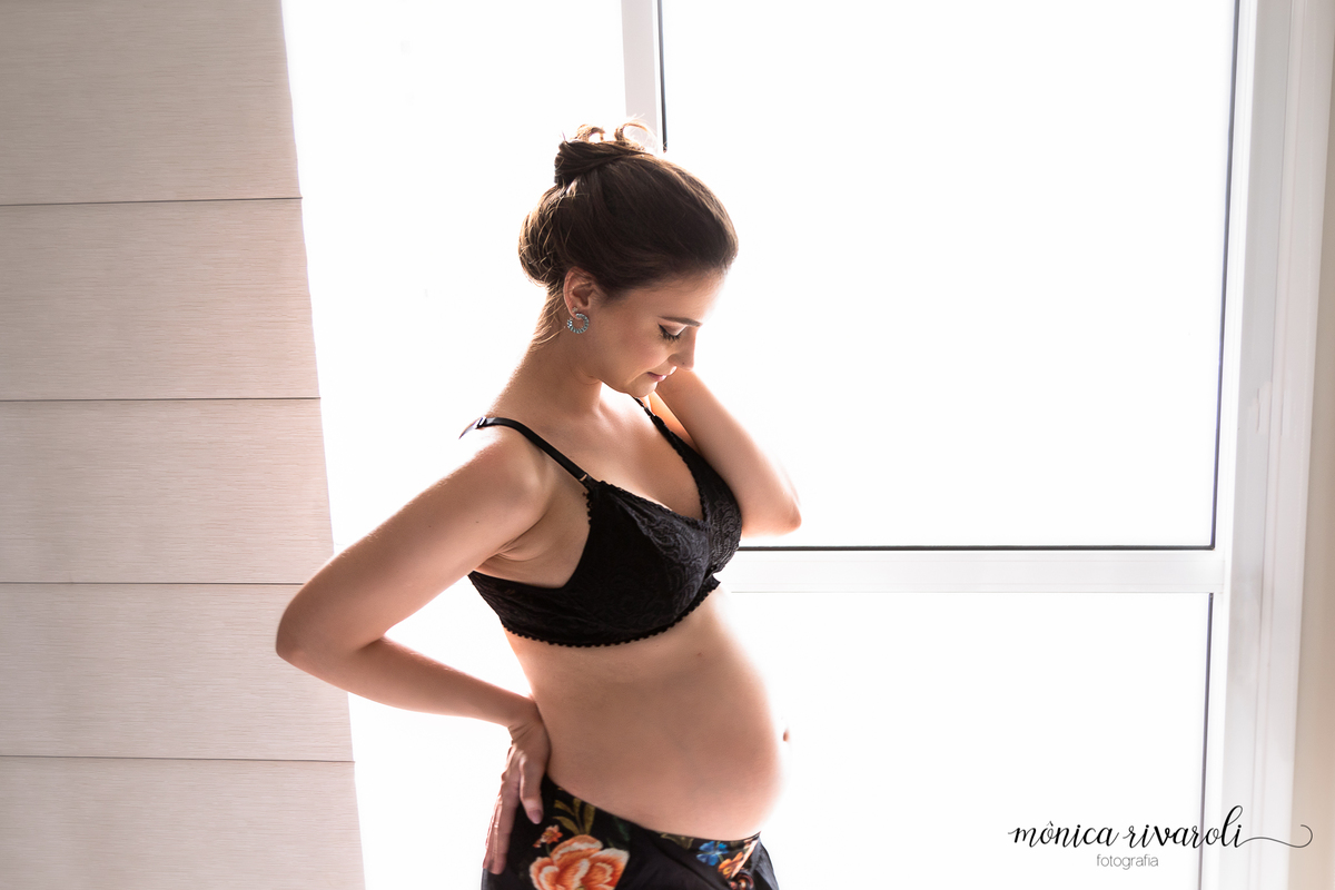 A mamãe Monica está na janela com os cabelos enrolados e presos segurando a emoção em sentir a bebê Victória se mexer!