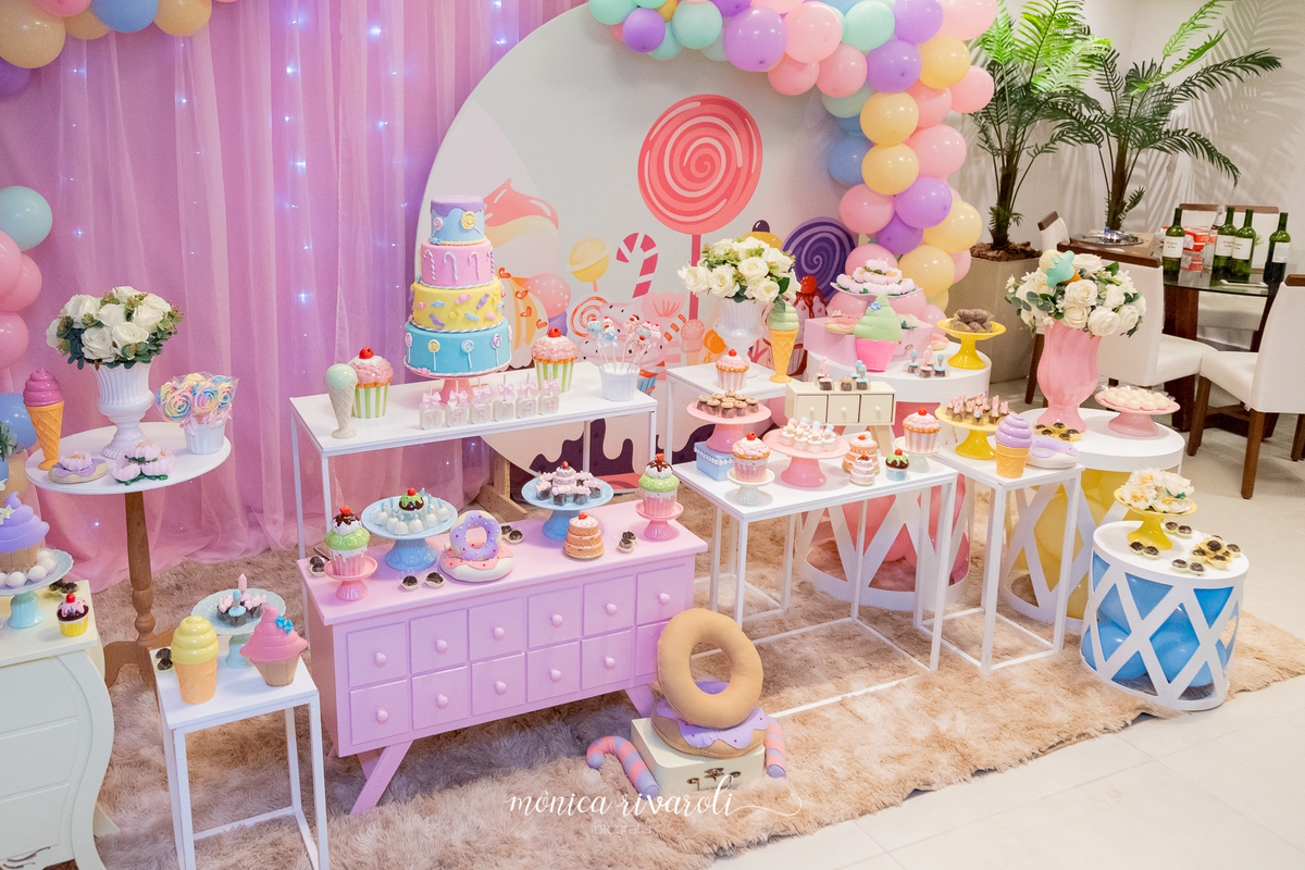 Lateral da mesa de doces. A decoração tem flores, docinhos, pirulitos e balões