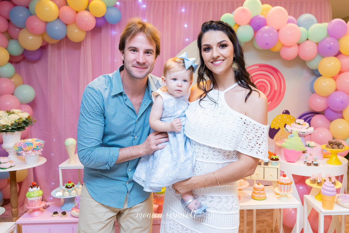 A Mariah está no colo da sua mãe e seu pai abraça as duas. Eles sorriem